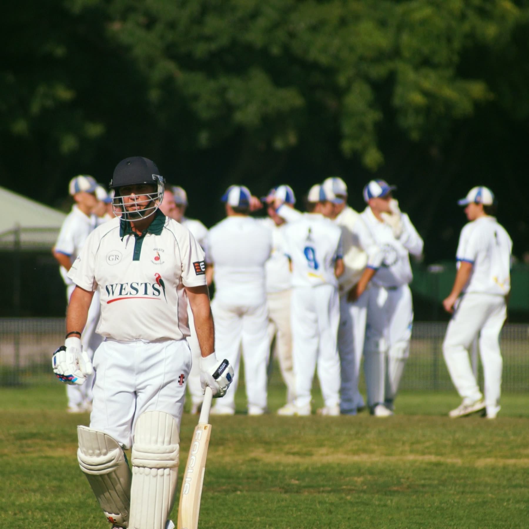 A batter walks back past the fielding side
